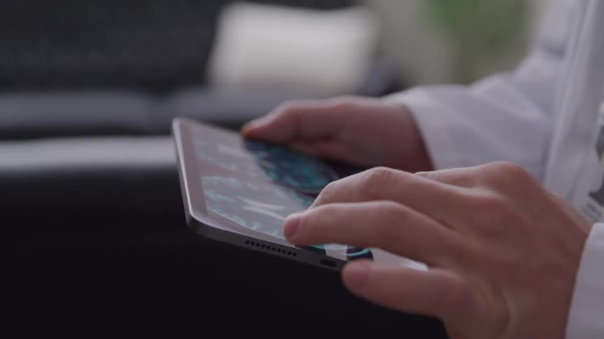 A closeup shot of a person in a white lab coat meticulously navigating a tablet displaying medical imagery