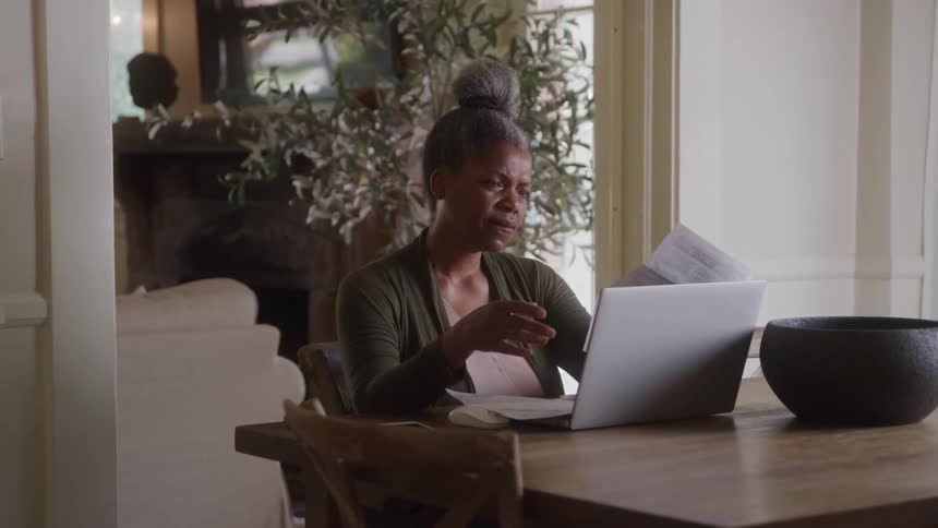 Woman analyzing documents while sitting at a desk in front of an open laptop