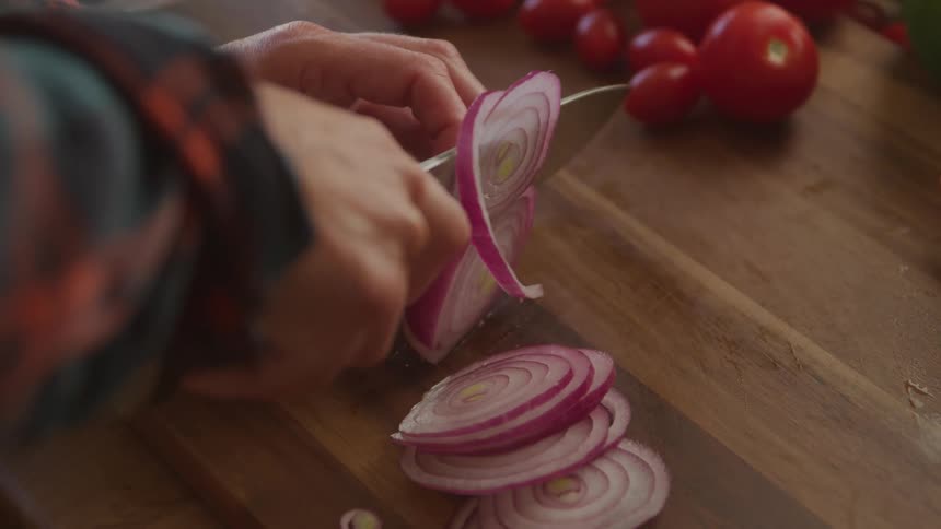 Hands with a knife cutting onion slices on a cutting board