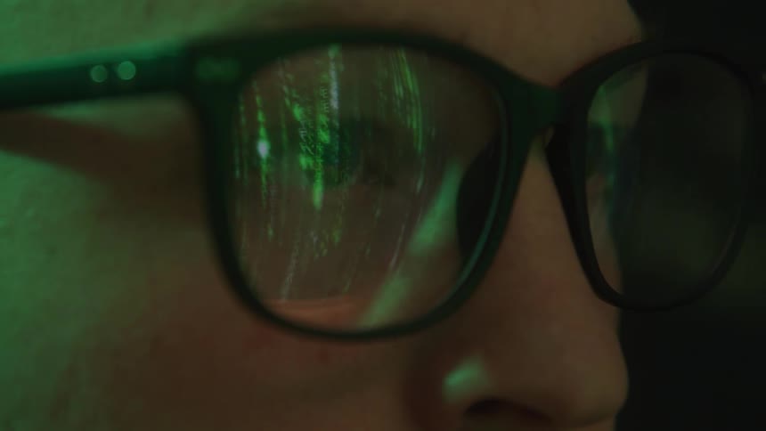 Closeup of a mans face with glasses reflecting code from a screen