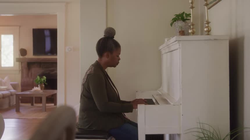 A woman plays the piano in her living room at midday