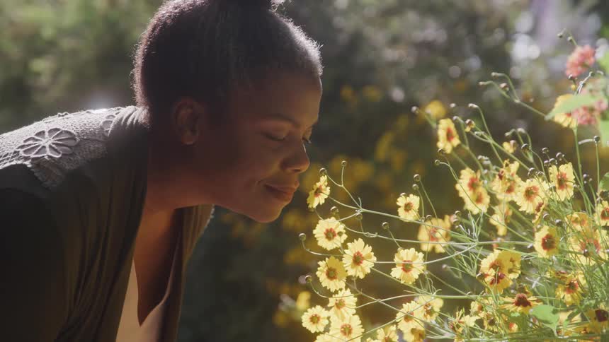 Woman in a backyard smelling yellow flowers