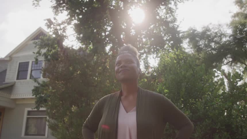 The woman i standing in front of her home smile