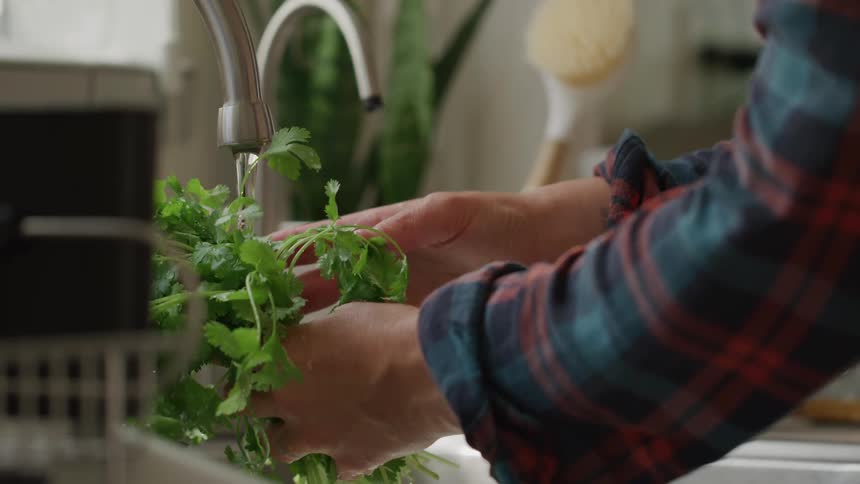 Close up of a woman washing green vegetables under running water in the kitchen during daytime
