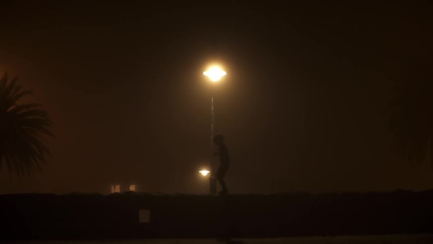 A figure walks in the dark past a lamp post