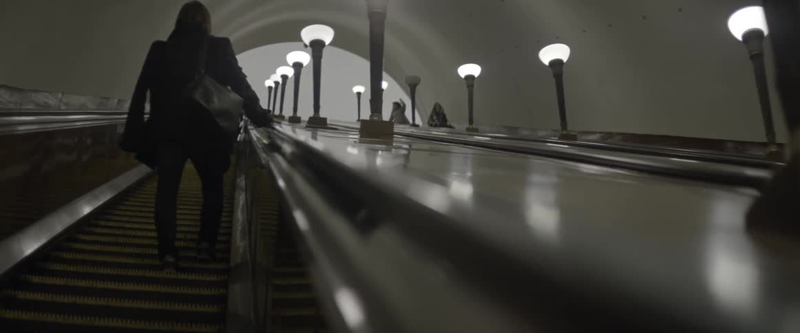A man rides up an escalator lined with lamps