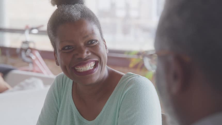 Close up of a black woman laughing while conversing with a middle aged black man in a room during daytime