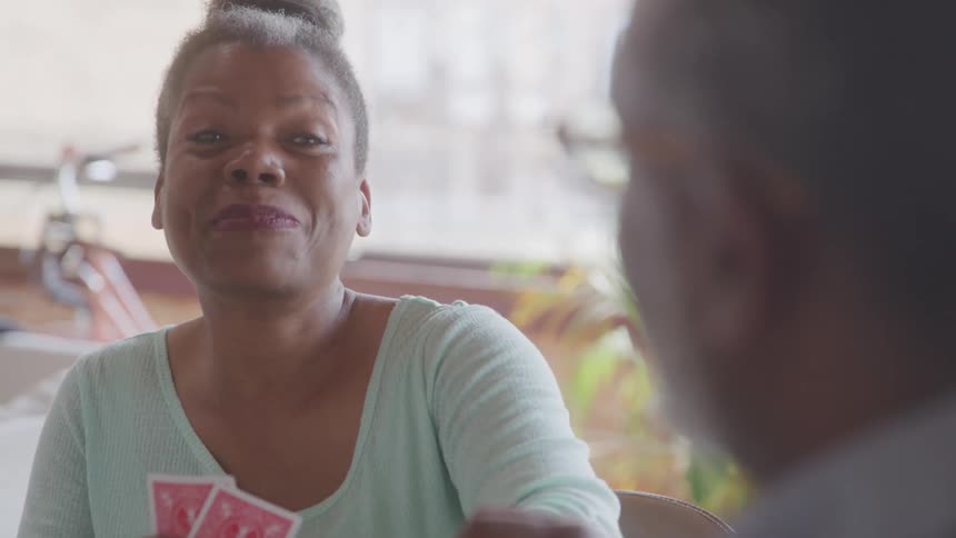 A smiling woman is playing cards with an unseen person appearing to be enjoying herself during the game she holds the cards in her hand and glances up with a broad grin