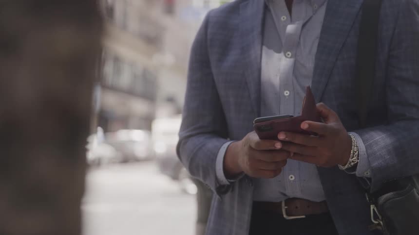 The man checks his phone on the street corner as cars pass by