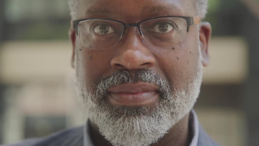 A black man with saltandpepper hair and glasses gazes calmly into the camera with a quiet confidence