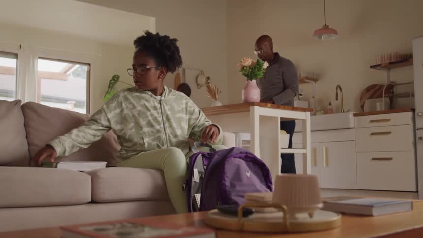 Girl waiting for school supplies in a backpack and in the background a man in the kitchen