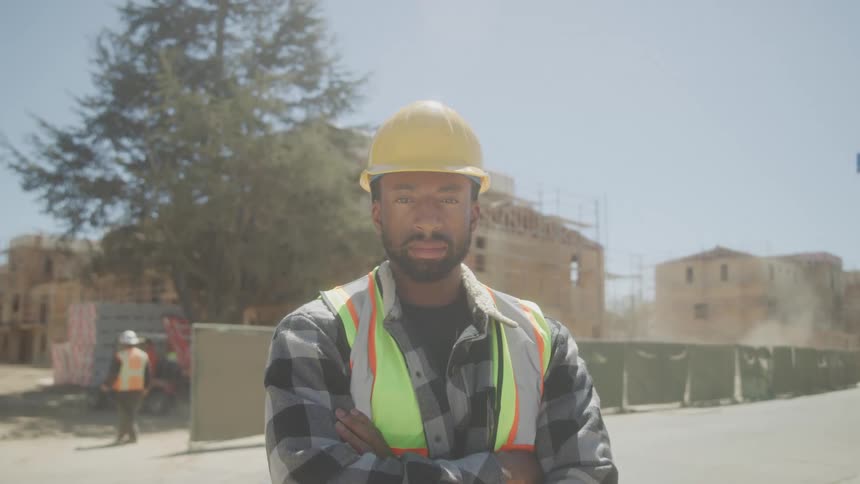 Male construction worker in hard hat and safety vest on construction site with arms crossed