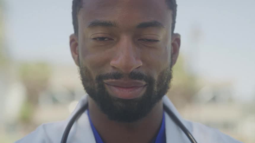 Close up happy male healthcare professional in white lab coat and stethoscope outdoors