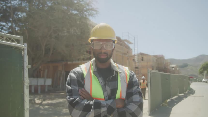 Male construction worker in hardhat safety vest and goggles on construction site with arms crossed