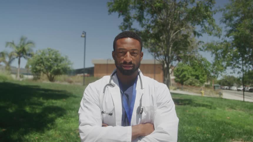 Doctor in white coat with arms crossed outdoors