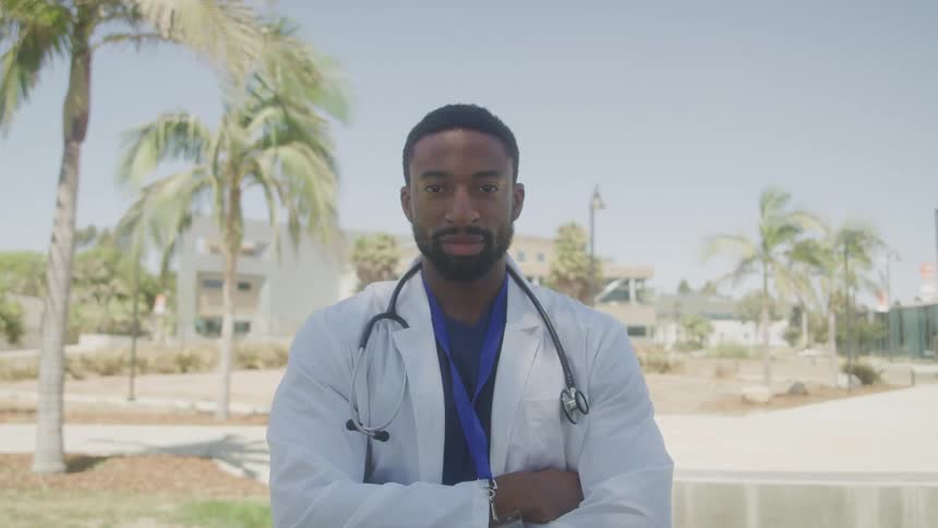 Outdoor portrait african american male medical professional with lab coat and stethoscope with arms crossed