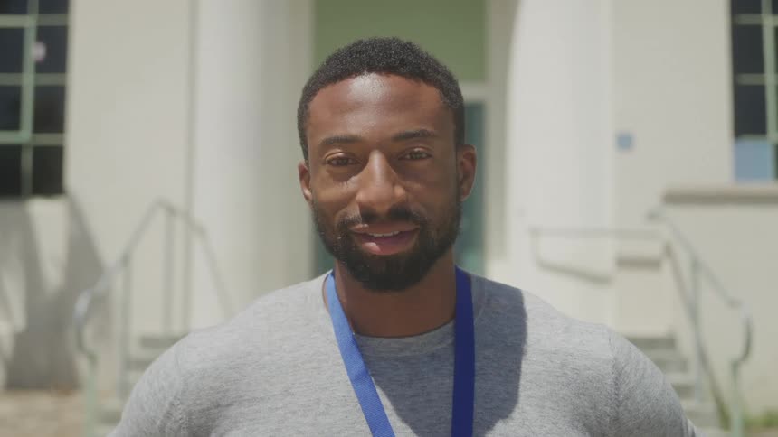 A smiling black man is standing outside near a building with stairs