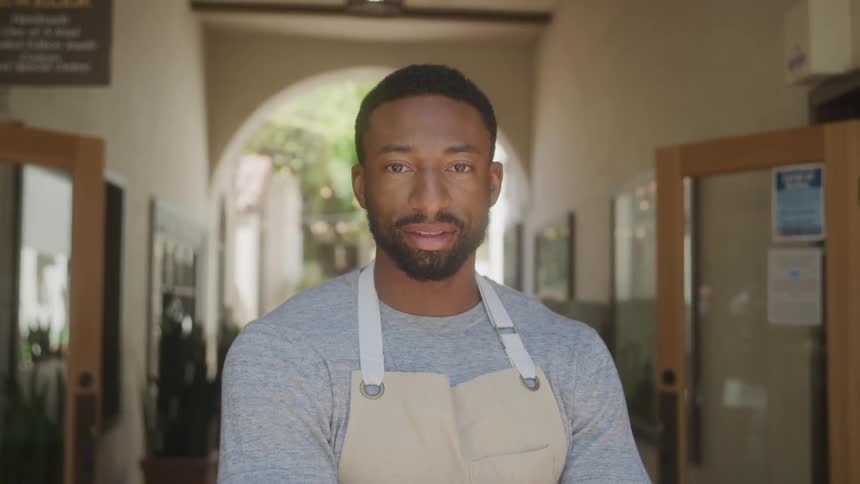 A man standing in a hallway wearing an apron at midday