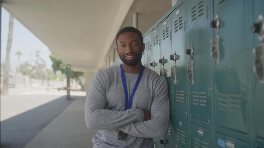 A man stands confidently by school lockers in an outdoor hallway