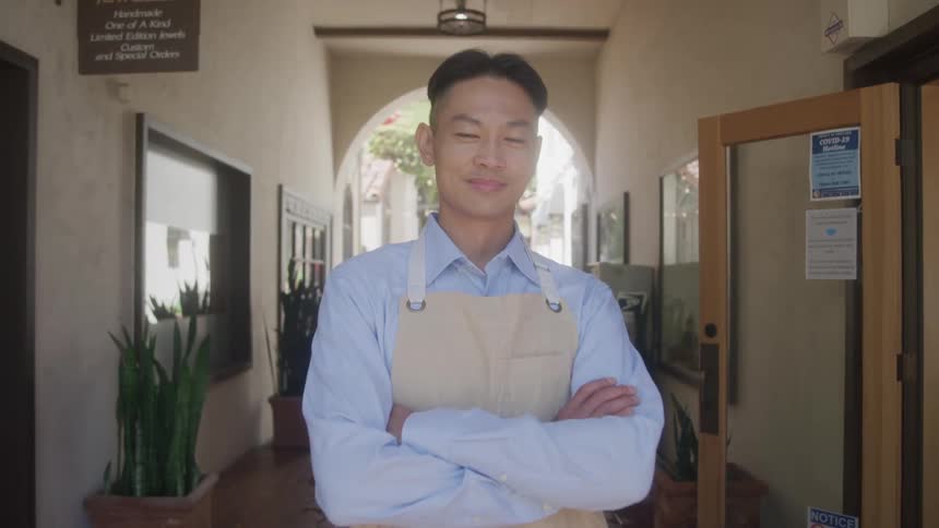 Man in apron stands confidently outside shop looking at camera