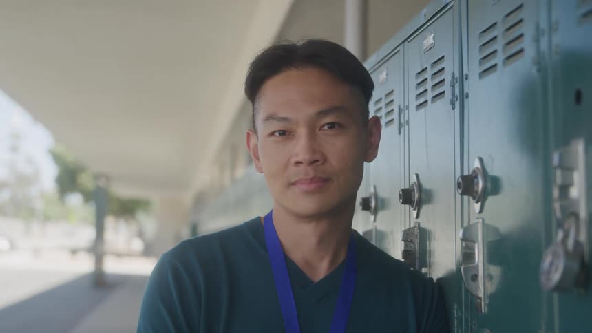 Man smiles while leaning against one of the lockers in a line of lockers located outside a building