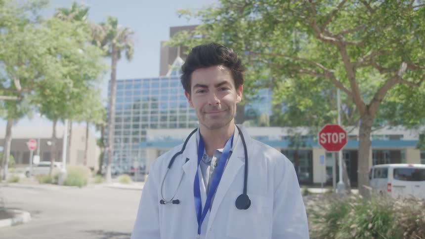 Close up of a young male doctor standing outdoors in a hospital park during daytime