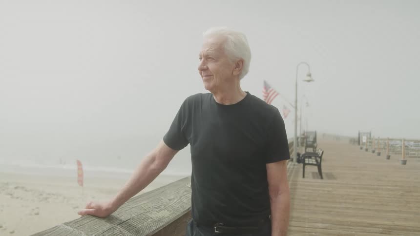 Elderly man enjoying the view of a beach on a pier