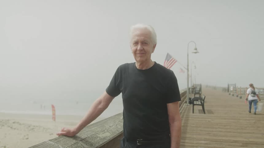 Elderly man with happy expression on a wooden bridge by the sea