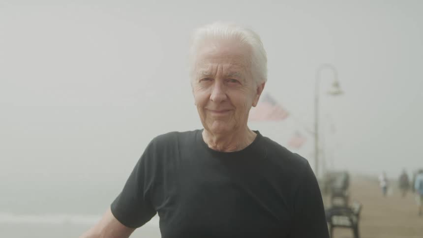 Elderly man standing near the rail on the boardwalk on a foggy day smiles
