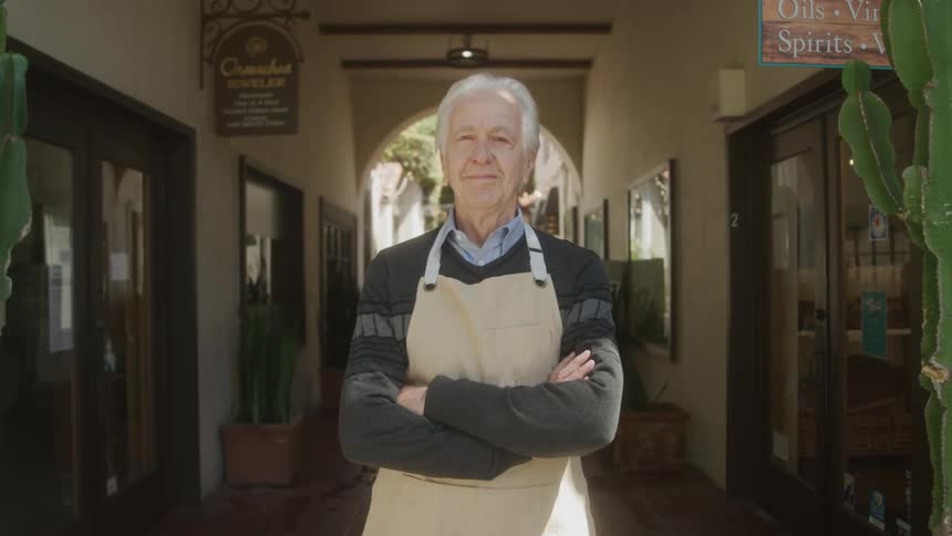 Elderly shopkeeper confidently faces camera outside his store
