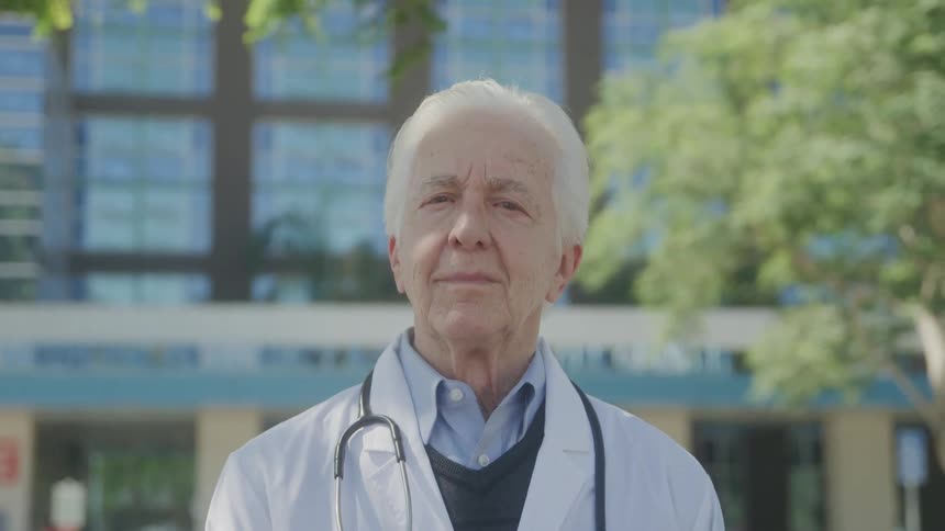 Close up portrait of an elderly male doctor standing outdoors during daytime