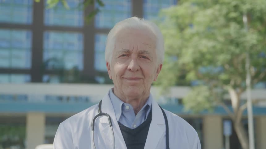 Close up portrait of an elderly male doctor standing outdoors during daytime