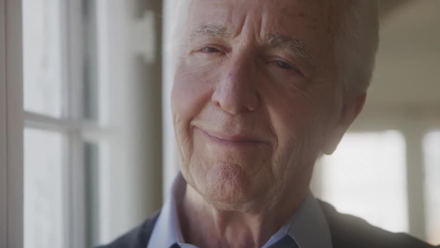 Close up portrait of an elderly man smiling while standing by the window in an office area during daytime