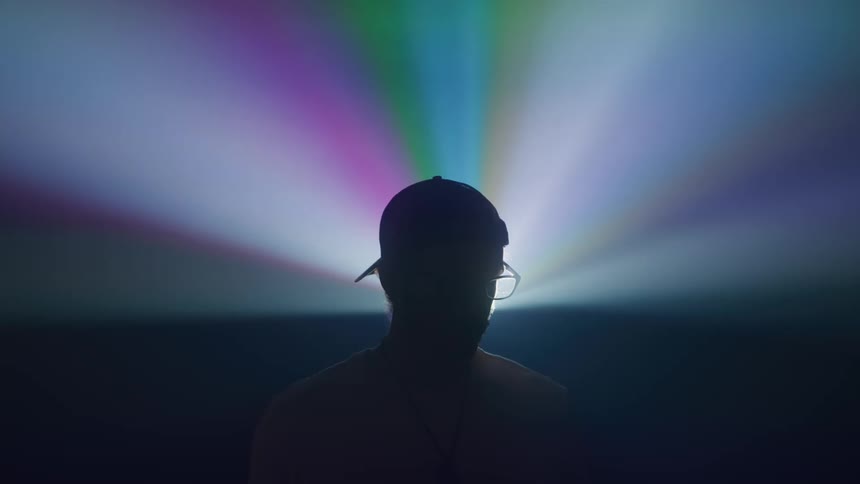 A man wearing a hat is in a nightclub with a dark atmosphere and flickering lights