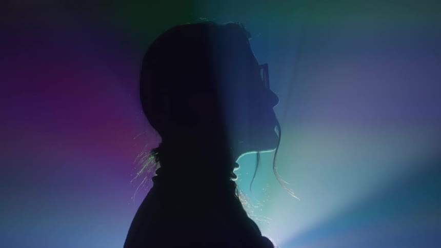 Silhouetted person stands against colorful lights
