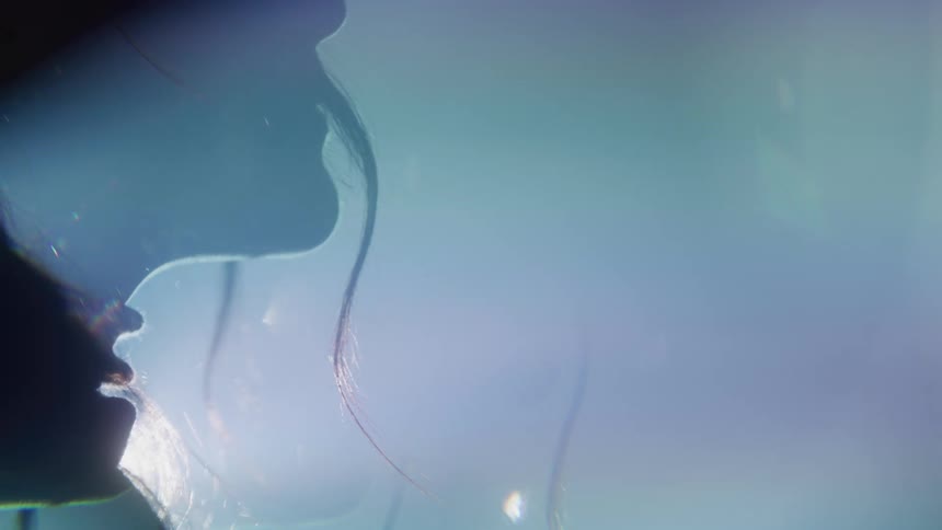 A young adult females face is seen in profile with long hair and glasses with bright lights behind her