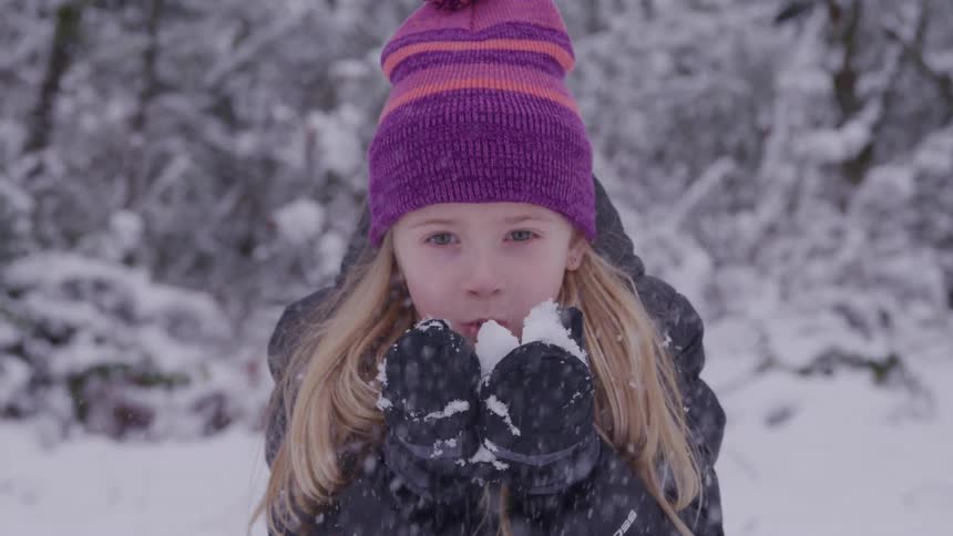 A girl blows snow ball in her palms while playing outdoors during daytime