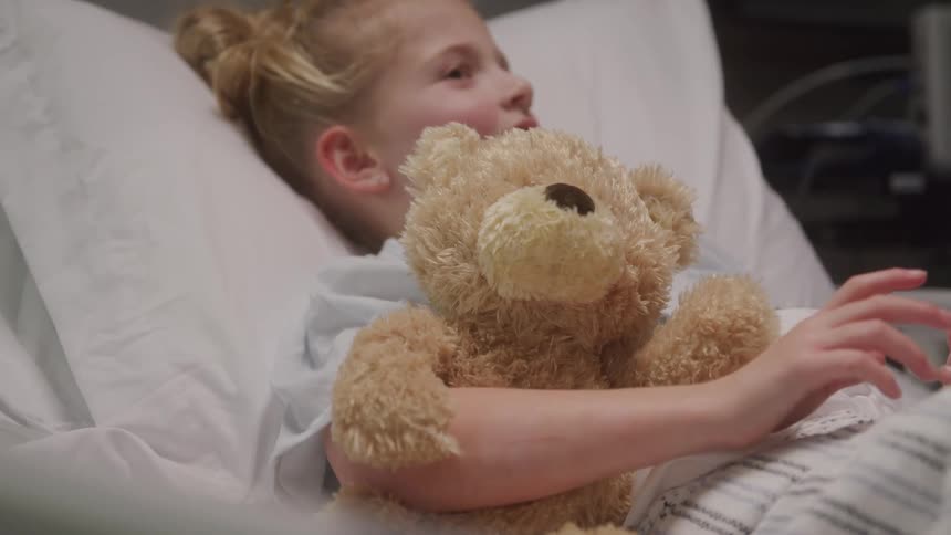 Little girl with a teddy bear lying in a hospital bed