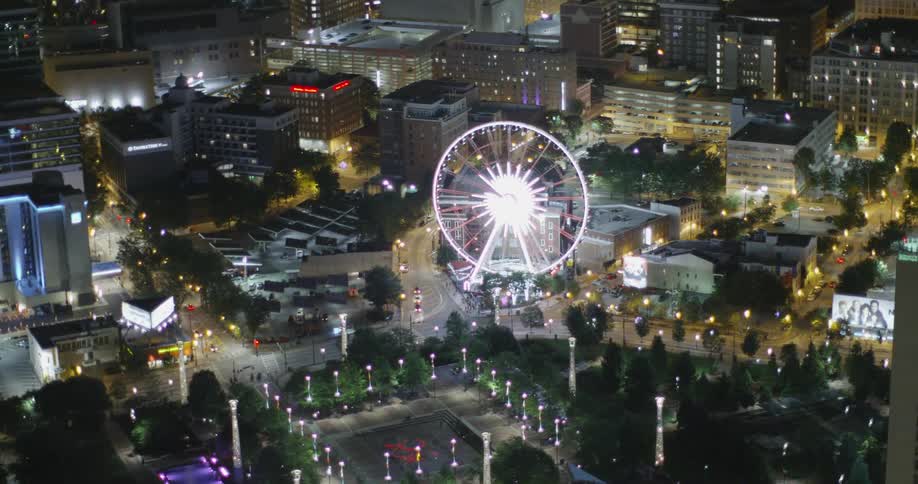 A large ferris wheel is lit at night in the middle of the city