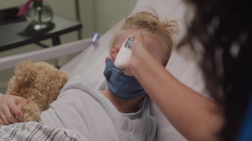 Nurse checking the temperature of a little girl lying in a hospital bed