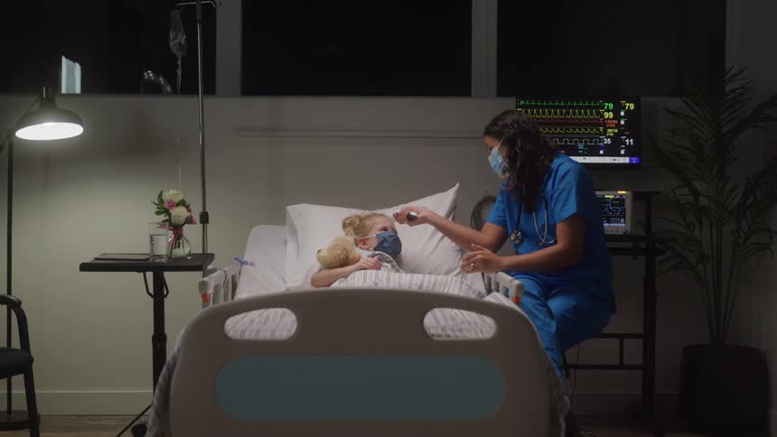 A nurse checks a child temperature in a hospital room at night