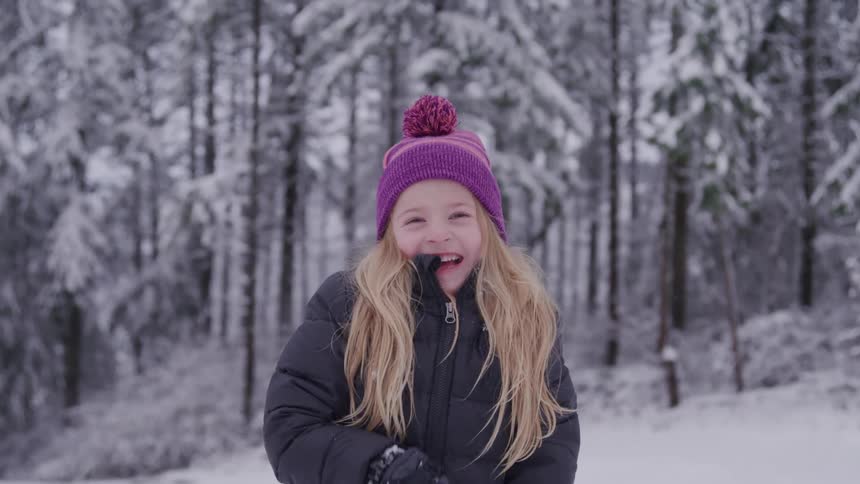 A young girl smiles while playing in a snowy forest