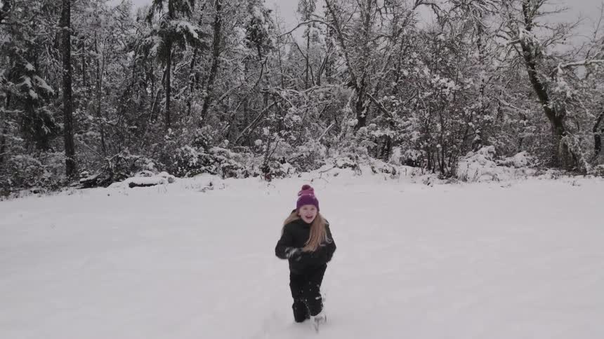 Little girl having fun running in the snow with a forest in the background