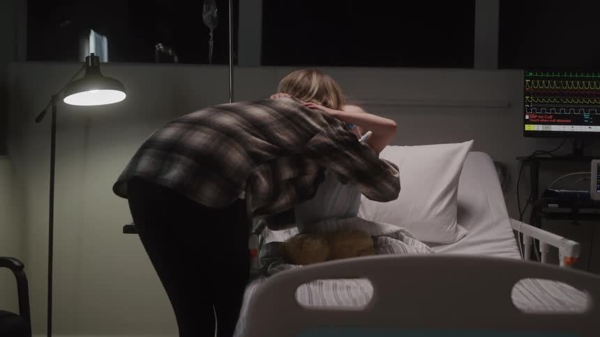 Mother hugging her little daughter who is sitting on a hospital bed at night