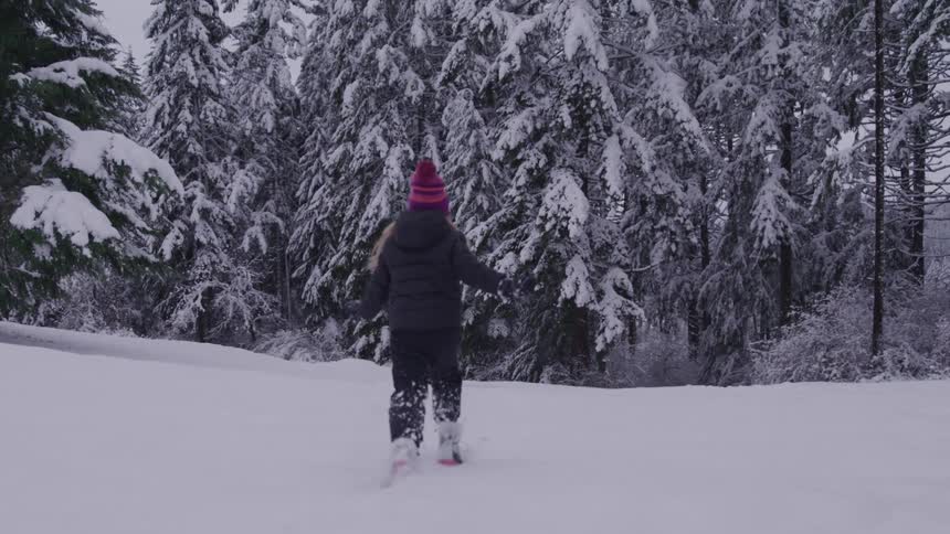 Little girl having fun running in the snow with trees in the background
