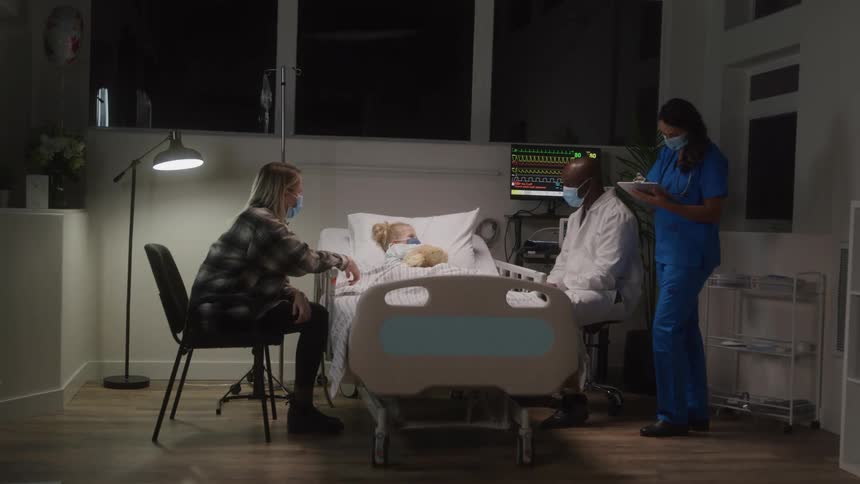 Medical staff accompanying a child who is sleeping in a hospital bed accompanied by his mother
