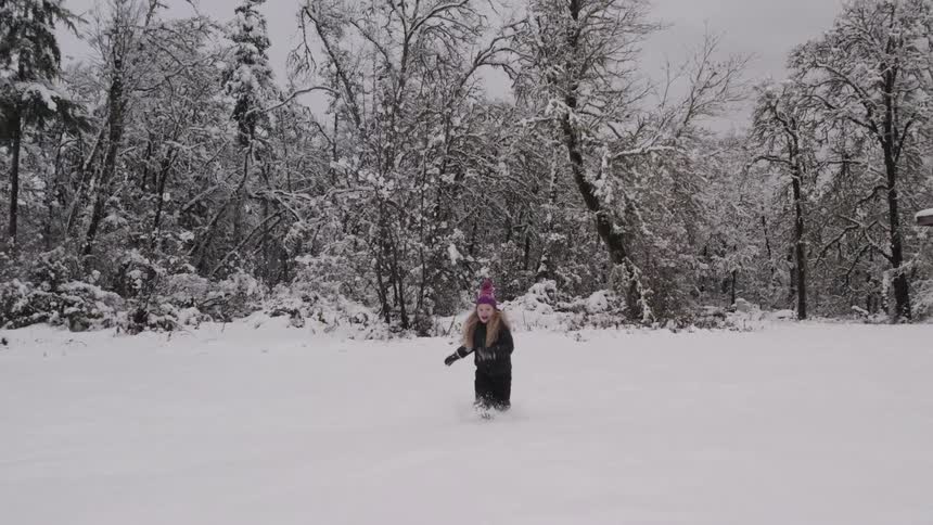 Little girl running in the snow with a forest in the background