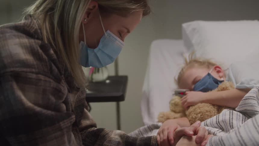 Mother with eyes closed sitting next to her little daughter who is sleeping in a hospital bed