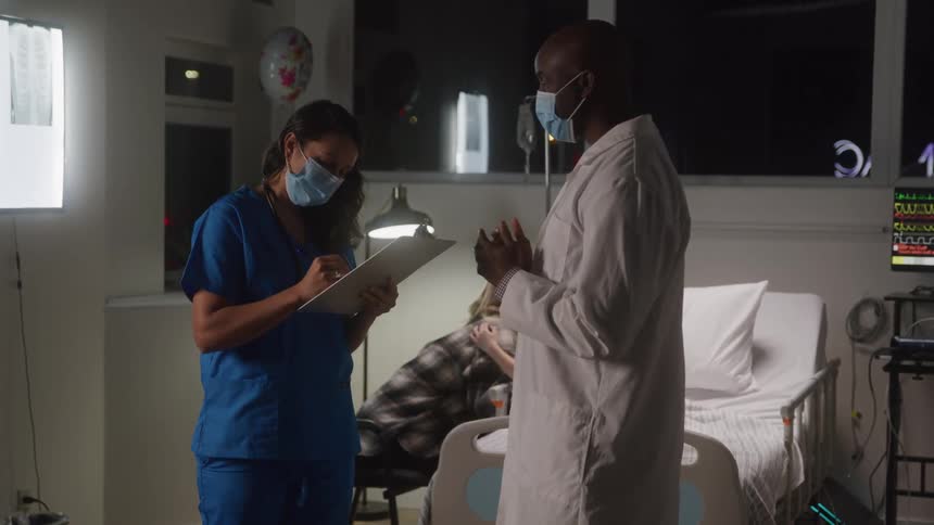 Doctor and a nurse talking in a hospital room with a patient lying down accompanied by an adult