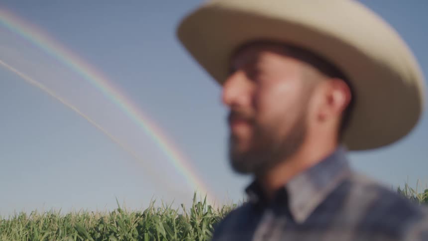 Man in a hat in the foreground of an agricultural field with a rainbow in the background